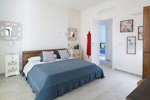 A bedroom with a large bed, bedside tables, a wardrobe, and a door leading to another room.