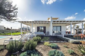 A modern house with a covered patio, a pool, and a landscaped garden.
