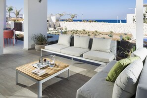 Zona d'estar exterior moderna amb un sofà i una taula de café, amb vista a una platja.