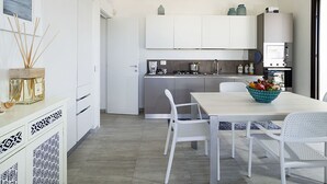Une cuisine moderne avec des meubles blancs, une table à manger entourée de chaises blanches et un saladier de fruits posé sur la table.
