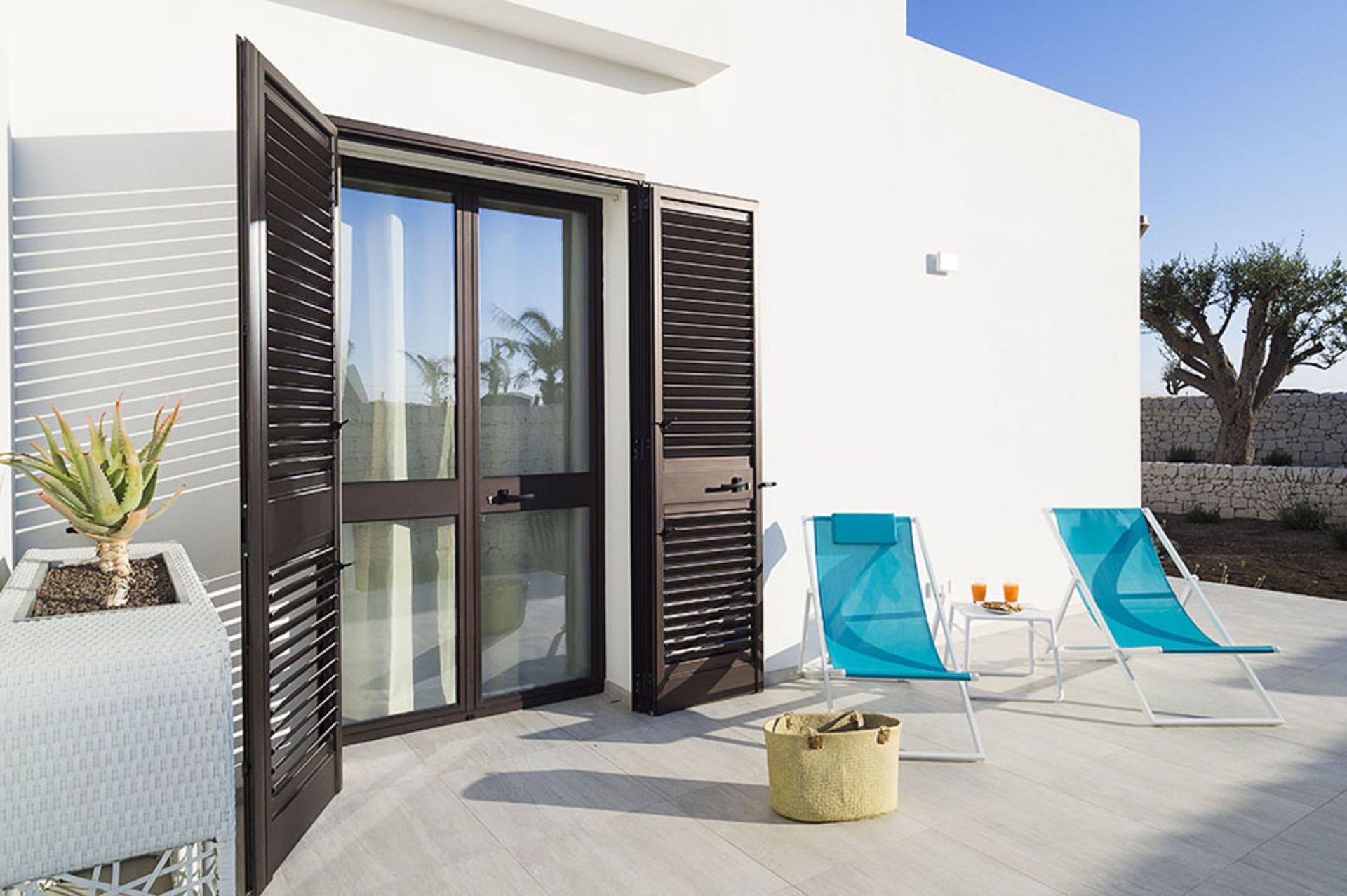 A modern outdoor area with a glass door, two blue lounge chairs, and a small plant.