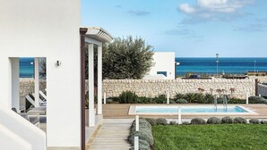 Un espace piscine extérieur moderne, agrémenté d’un mur en pierre et offrant une vue sur la mer.
