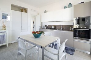 A modern kitchen with white cabinetry, a wooden dining table, and two white chairs.