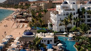 Un complex turístic amb platja, piscina i un paisatge de muntanyes al fons.