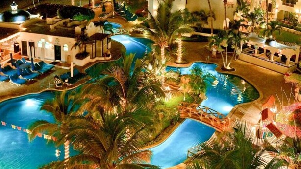 Un complex turístic amb diverses piscines, palmeres i una zona d'estar ben il·luminada.