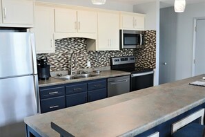 A modern kitchen with white cabinets, a stainless steel refrigerator, a microwave, and a tiled backsplash.