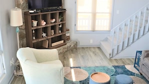 A living room with a television, a bookshelf, a sofa, a window, and a staircase.