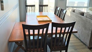 A dining area with a wooden table and chairs, a tray on the table, and a view of the ocean through large windows.
