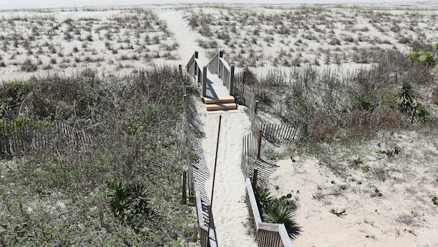 A sandy beach with a wooden boardwalk leading to the water.