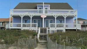 A two-story beach house with a balcony, a sign reading 'Quarter Deck,' and a wooden fence in front.