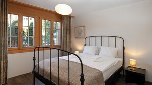 Ein Schlafzimmer mit einem Himmelbett, einem Fenster mit Vorhängen, einer Nachttischlampe und einem gerahmten Bild an der Wand.