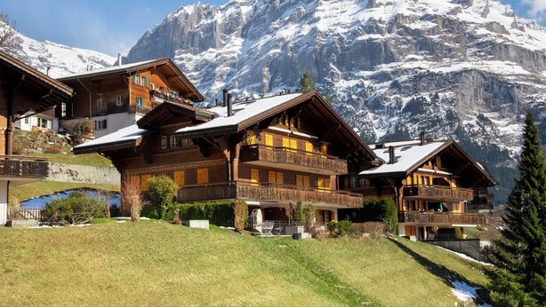 Ein Chalet-Hotel mit mehreren Balkonen vor einer verschneiten Berglandschaft.