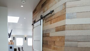 Een modern interieur met een schuifdeur, houten wandpanelen, een grijs vloerkleed en een eethoek met stoelen.