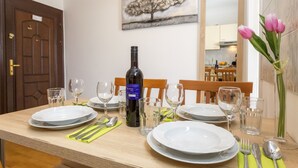 Une table à manger dressée avec des assiettes, des couverts et une bouteille de vin, et un vase de fleurs placé sur le côté droit.