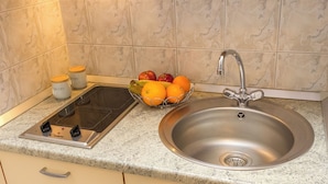 Une cuisine équipée d’un évier en acier inoxydable, d’un panier à fruits contenant des oranges et des pommes, et de deux pots à épices.