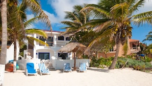 Een hotel aan het strand met een zwembad, palmbomen en een rieten constructie.