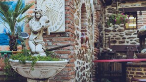 Un muro de piedra con una estatua de una mujer sosteniendo un caballo, un girasol y una jardinera con follaje.