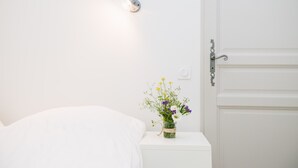 Una mesita de noche blanca con un pequeño florero, una pared blanca y una puerta con picaporte plateado.