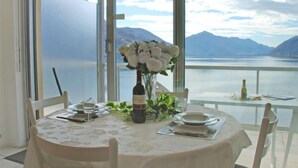 Una mesa de comedor con mantel blanco, una botella de vino y un ramo de flores blancas. La mesa está dispuesta para dos personas, con platos, cubiertos y copas.
