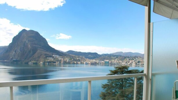 Un balcón con vistas despejadas a un lago, montañas y un pueblo al fondo.