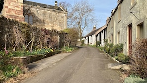 A narrow street flanked by stone buildings with arched windows and a stone wall with flowering plants. - Kirkside Cottage pet friendly, sleeps 4 near St Andrews (Upper Largo)