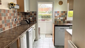 A kitchen with a tiled backsplash, a built-in dishwasher, and a window with a view of the outside. - Kirkside Cottage pet friendly, sleeps 4 near St Andrews (Upper Largo)