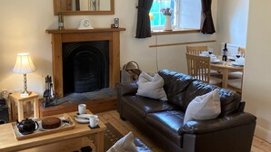 A cozy living room with a fireplace, a dining table set for two, and a comfortable leather sofa. - Kirkside Cottage pet friendly, sleeps 4 near St Andrews (Upper Largo)