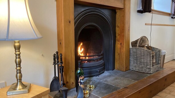 A cozy room with a stone fireplace, a lamp, a bottle of whisky, and a wicker basket. - Kirkside Cottage pet friendly, sleeps 4 near St Andrews (Upper Largo)