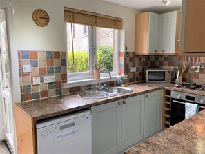 A modern kitchen with a built-in dishwasher, a sink with a window above, a microwave, and a stove.