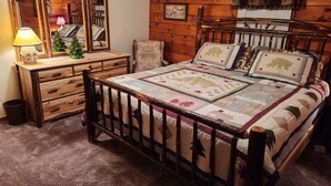 A cozy bedroom with a wooden four-poster bed, a dresser with a mirror, and a small Christmas tree.