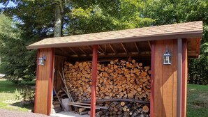 A wooden structure with a roof, containing a stack of firewood and two lantern-style lights.