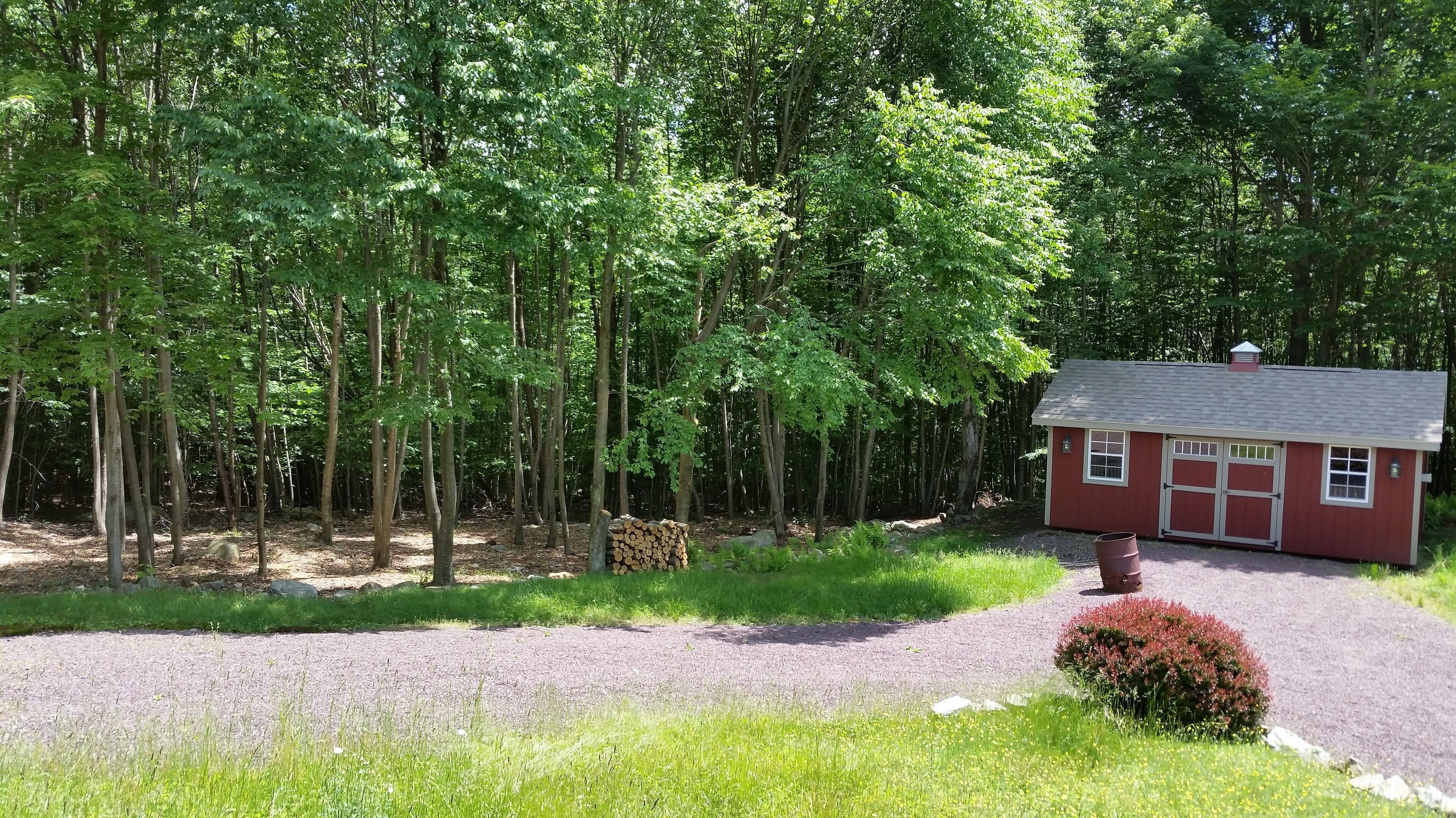 Une petite cabane rouge avec une allée en gravier et une zone boisée en arrière-plan.