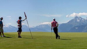 A golf course with players in motion, a clear sky, and mountains in the background.