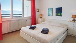 A bedroom with a bed, two bedside tables, a window with a view, and two wall-mounted paintings.
