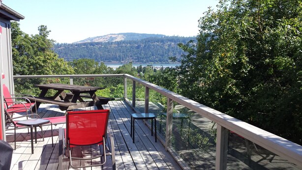 A wooden deck with a picnic table and chairs, overlooking a lake and hills. - Quaint & cozy home in DT Hood River, AMAZING Views off the privacy deck (Hood River)
