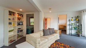 A living room with a sofa, a bookshelf, a small table, and a potted plant. - Quaint & cozy home in DT Hood River, AMAZING Views off the privacy deck (Hood River)