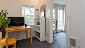A room with a wooden desk, a television, a bookshelf, and a door leading to another room. - Quaint & cozy home in DT Hood River, AMAZING Views off the privacy deck (Hood River)