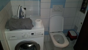 Un baño pequeño con lavadora, inodoro y un estante sobre el inodoro.