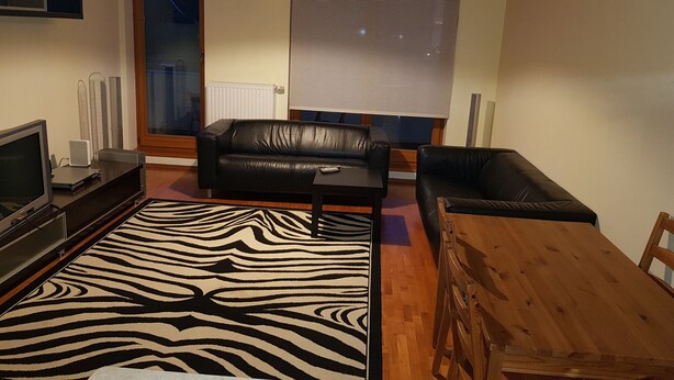 Una sala de estar con un tapete estampado de cebra, dos sofás de cuero negro, una mesa de comedor de madera y un televisor sobre un mueble bajo.