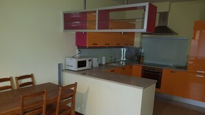 Una cocina compacta con microondas, hervidor de agua y pileta. Hay una mesa de comedor de madera con sillas.