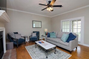 A living room with a sofa, two armchairs, a coffee table, a ceiling fan, and a window with blinds.