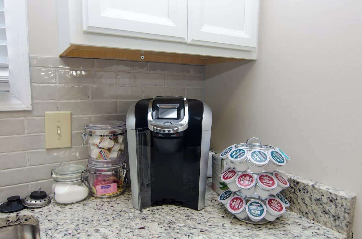 A kitchen with a coffee maker, jars of food, and a stack of yogurt containers.