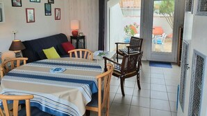 A room with a dining table, chairs, a sofa, and a view through a glass door to the outside. - 2 rooms apartment entirely renovated of 36 m2 (Noirmoutier-en-l'Île)