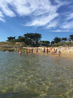 Una playa con aguas poco profundas y cristalinas, gente tomando el sol y árboles al fondo.