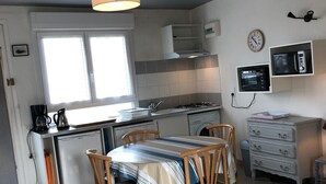 A compact kitchen with a dining area, a refrigerator, a microwave, and a clock on the wall. - 2 rooms apartment entirely renovated of 36 m2 (Noirmoutier-en-l'Île)