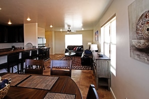 A modern kitchen with dark cabinets, a dining area with a wooden table and chairs, a living room with a sofa and a coffee table, and a large window providing natural light. - 13A1 Delicate Arch Delight (Moab)
