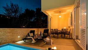 A poolside area with lounge chairs and a dining table, a small table with candles, and a brick wall. - Luxury Villa LeLu with heated saltwater pool suitable for children and pets, with parking, high speed Internet, BBQ (Žrnovnica)