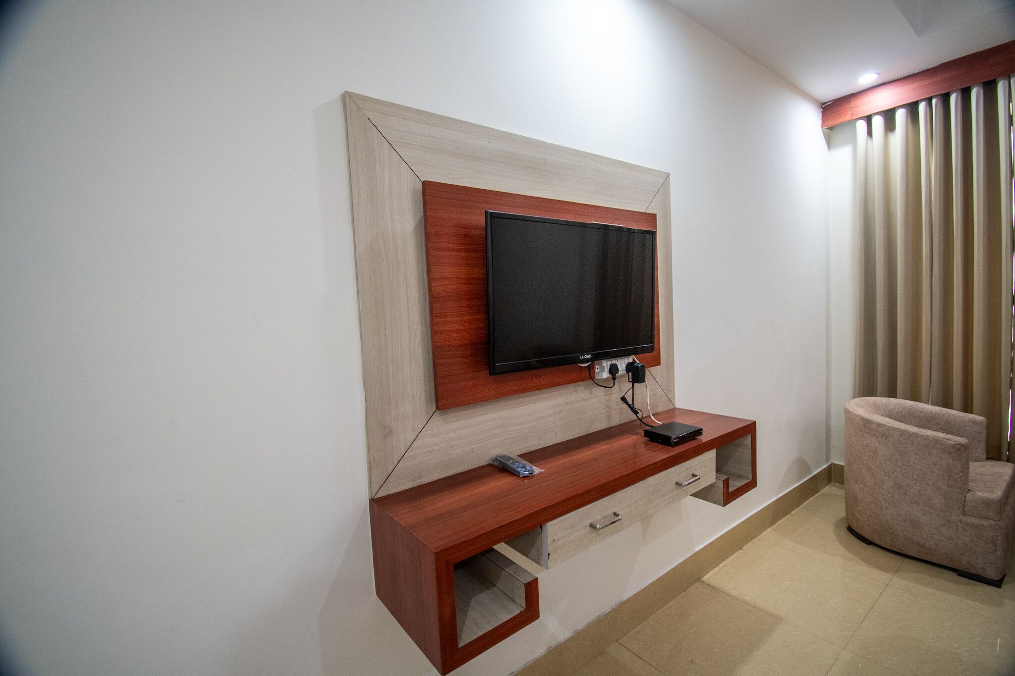 Un salon moderne avec un téléviseur fixé au mur, une console en bois et un fauteuil confortable.