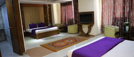 A hotel room with a large bed, a television, a sofa, and a desk.