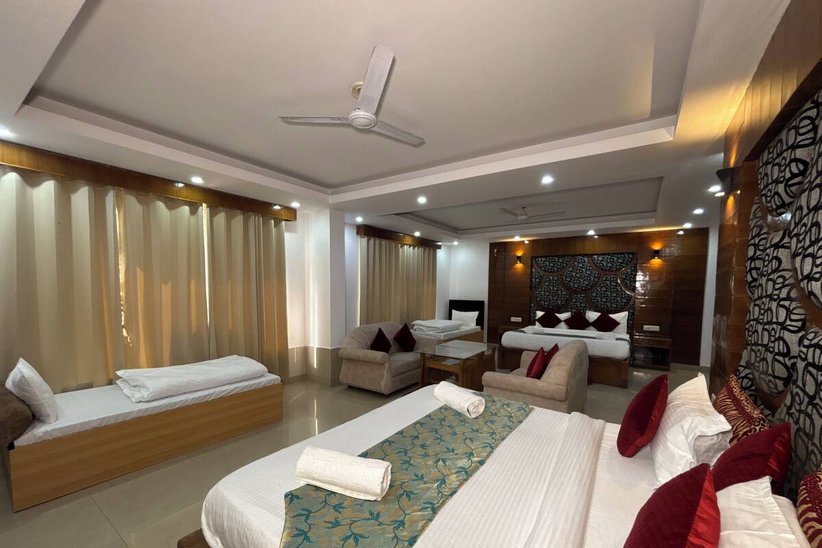 A hotel room with two beds, a sofa, a small table, and a ceiling fan.